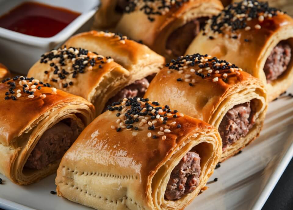 Golden Sausage Rolls Topped with Everything Bagel Sea Salt served in a White Dish