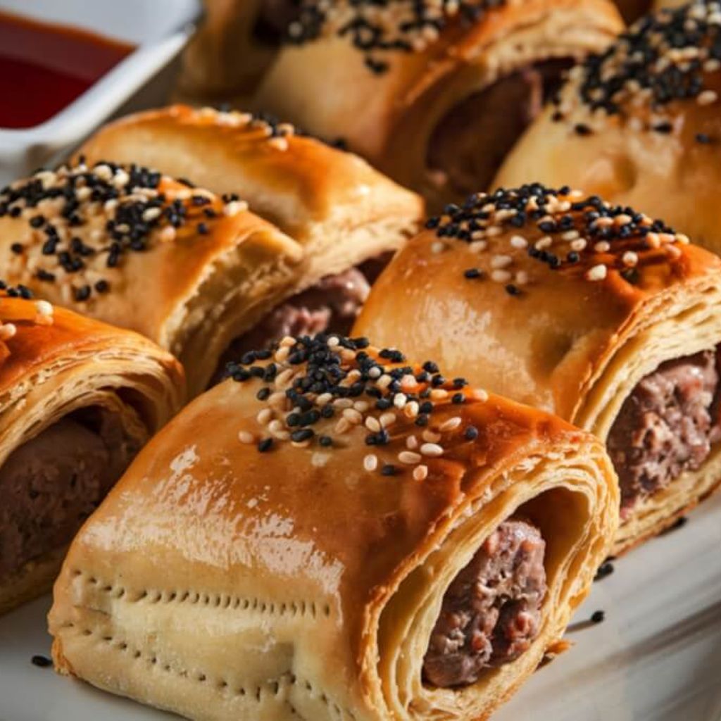 Golden Sausage Rolls Topped with Everything Bagel Sea Salt served in a White Dish