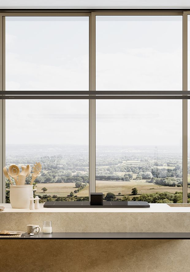 Lighting rail suspended horizontally over a kitchen island, positioned in front of a large window with a panoramic countryside view.