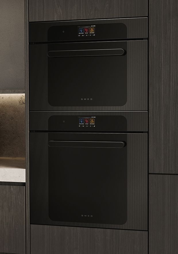 wo built-in black ovens built-in vertically within dark wood kitchen cabinetry.