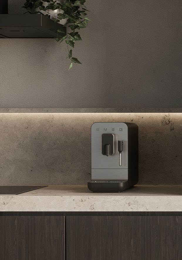 Compact coffee machine placed on a stone countertop beneath a wall shelf with hanging greenery.