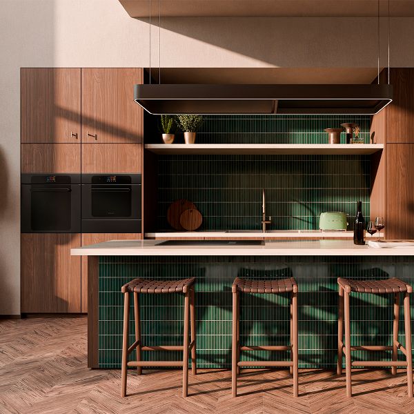 A kitchen featuring wood cabinets, black built-in ovens, and a white marble island with green vertical tiles and woven leather stools.