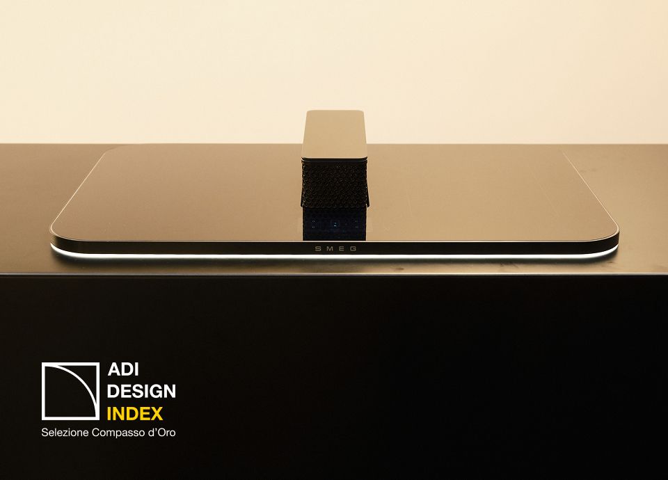 SMEG Isola induction hob with integrated extraction system, displayed on a minimalist black countertop, featured in the ADI Design Index.
