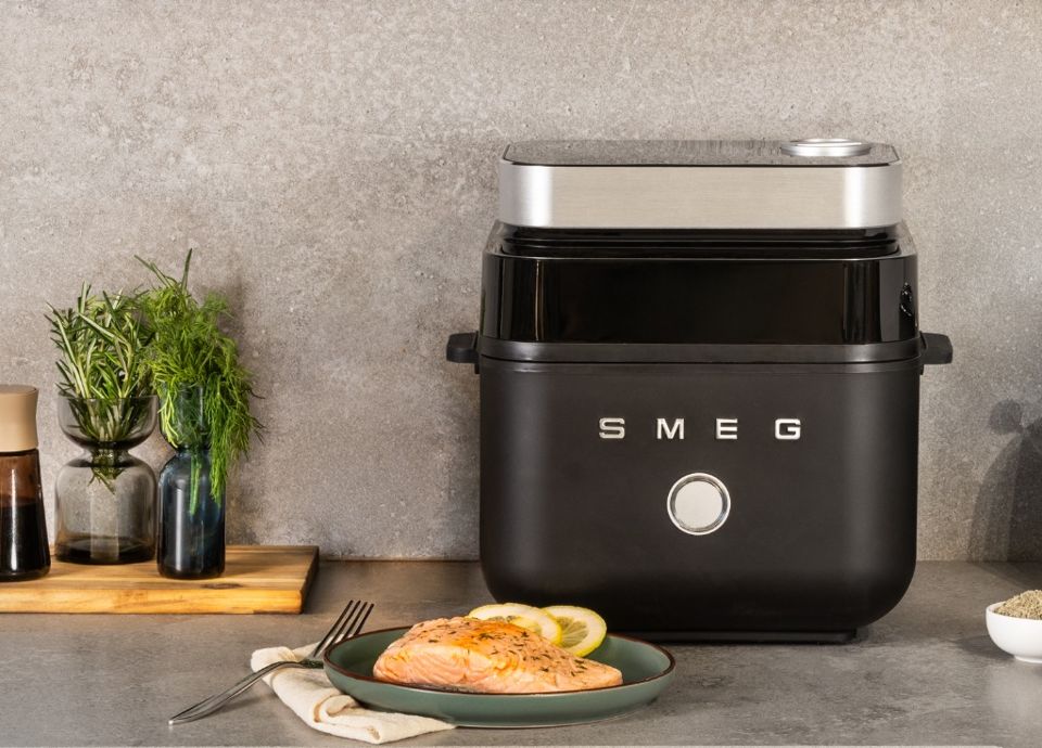 SMEG airfryer in matzwarte uitvoering met een bereid gerecht op een keukenaanrecht.