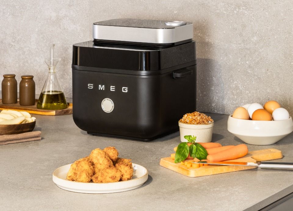 Black SMEG air fryer on a kitchen countertop with crispy fried food and fresh ingredients