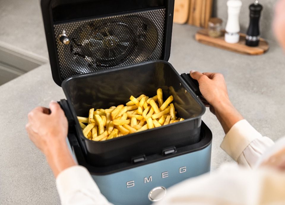 Smeg air fryer with open basket filled with crispy fries on a kitchen countertop