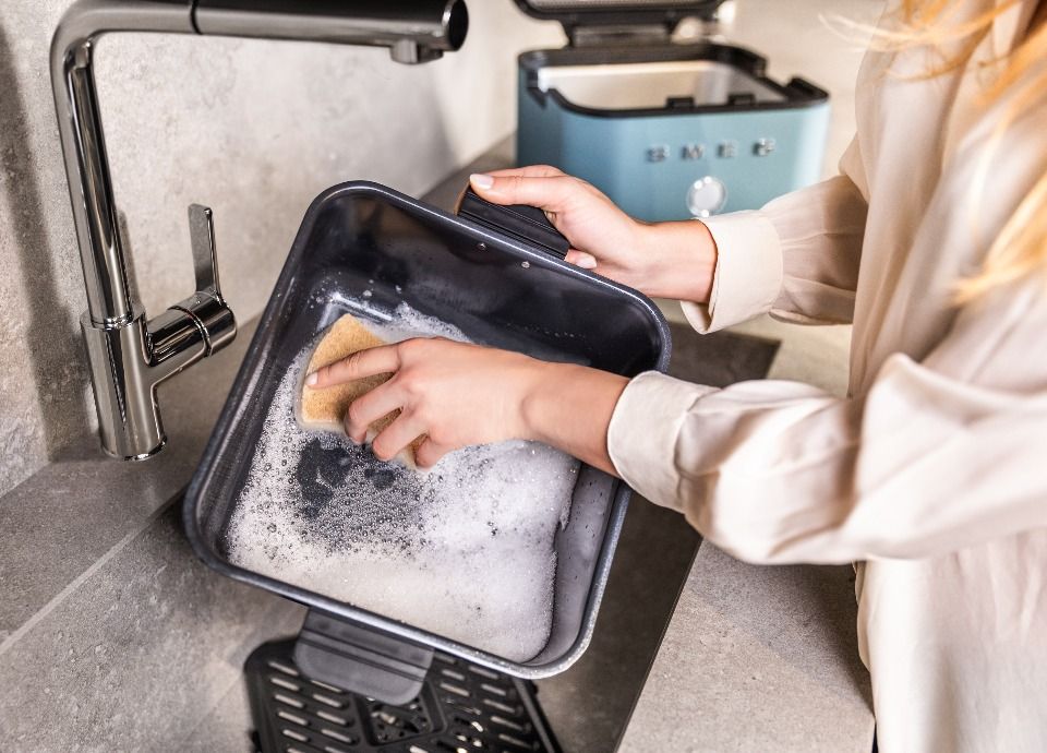 Smeg air fryer basket being washed in the sink with sponge and water