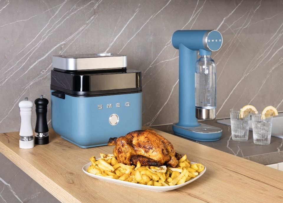 Smeg blue air fryer on a wooden countertop with roasted chicken and potatoes in a modern kitchen setting