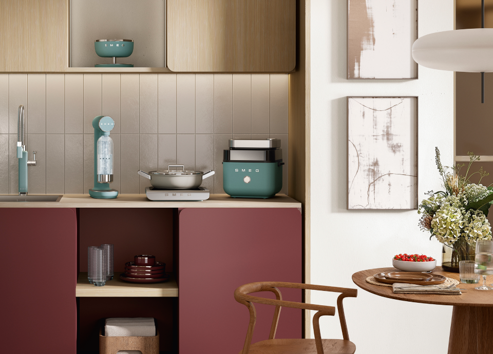 Smeg emerald green air fryer on a kitchen countertop with light wood cabinets, neutral wall panels and coordinated small appliances