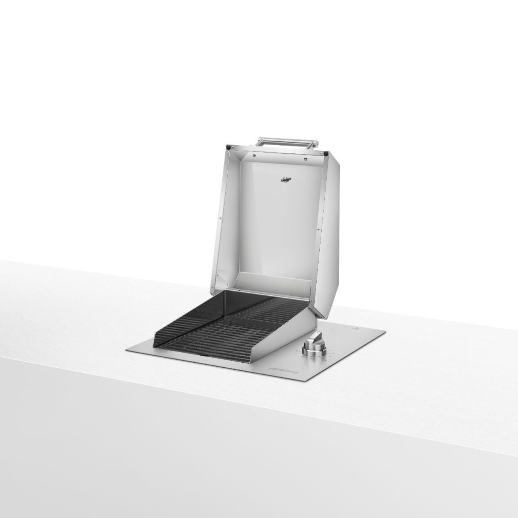 Built-in stainless steel barbecue with open lid. The cooking surface features black cast-iron grates. On the right side, there is one round metal knob for temperature control. The design is sleek and modern, with a polished finish and sturdy details. The appliance is placed on a light-colored countertop.