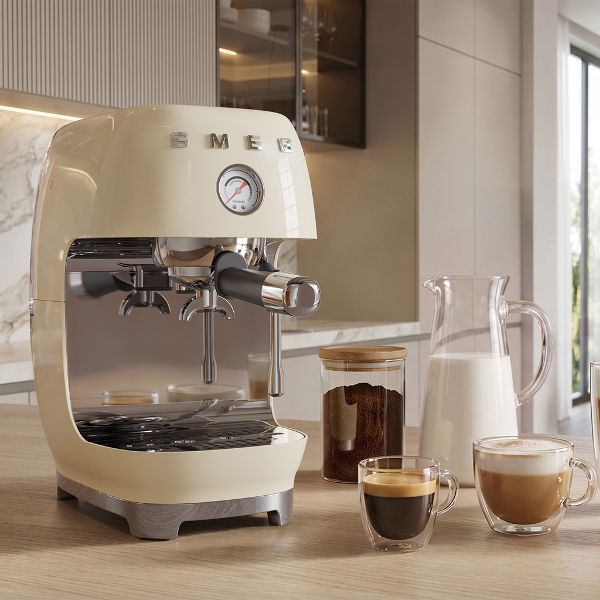 Cafetera Espresso Manual SMEG ECF03CREU con un café espresso y un café con leche en una cocina en tonos tierra claros.