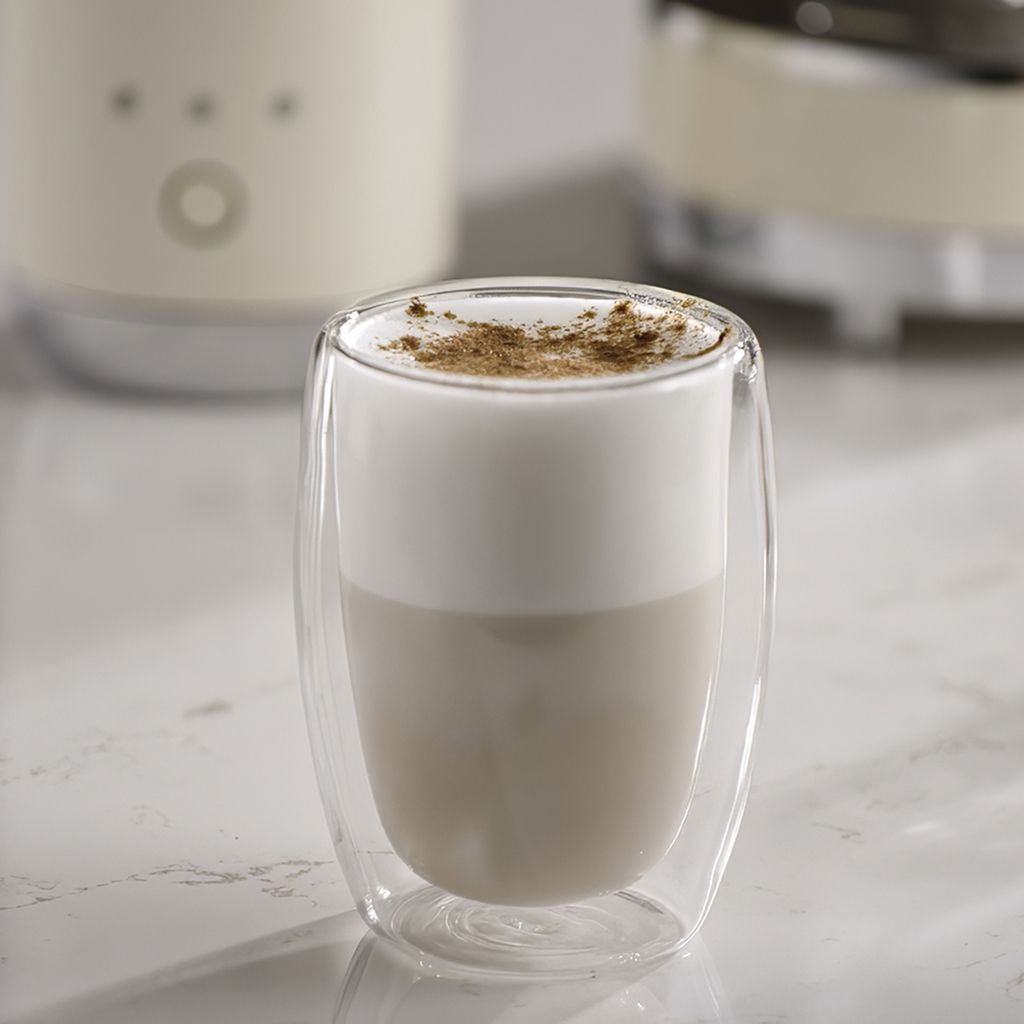 A layered iced cappuccino served in a double-walled glass, with creamy foam topped with a light dusting of cocoa.