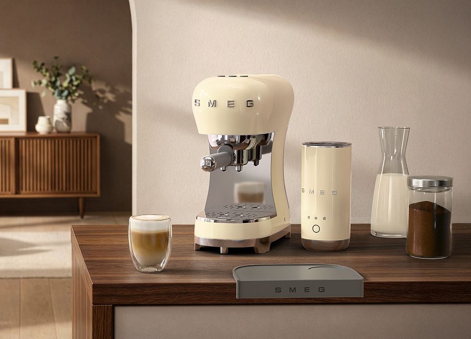 ream SMEG espresso machine with matching milk frother coffee set on a wooden countertop with a latte glass, milk carafe, and coffee grounds jar in a modern kitchen setting