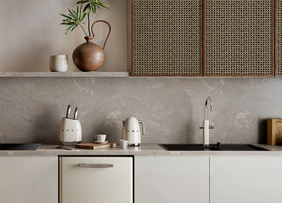 Contemporary kitchen tap with a sleek chrome finish mounted on a beige stone countertop beside a black integrated sink.