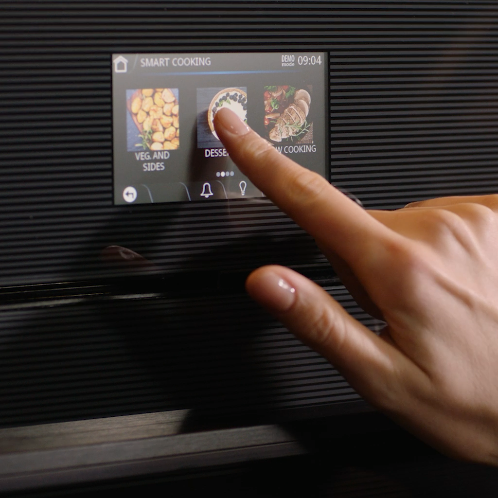 Hand interacting with a oven touchscreen displaying Smart Cooking programs and food categories​‌