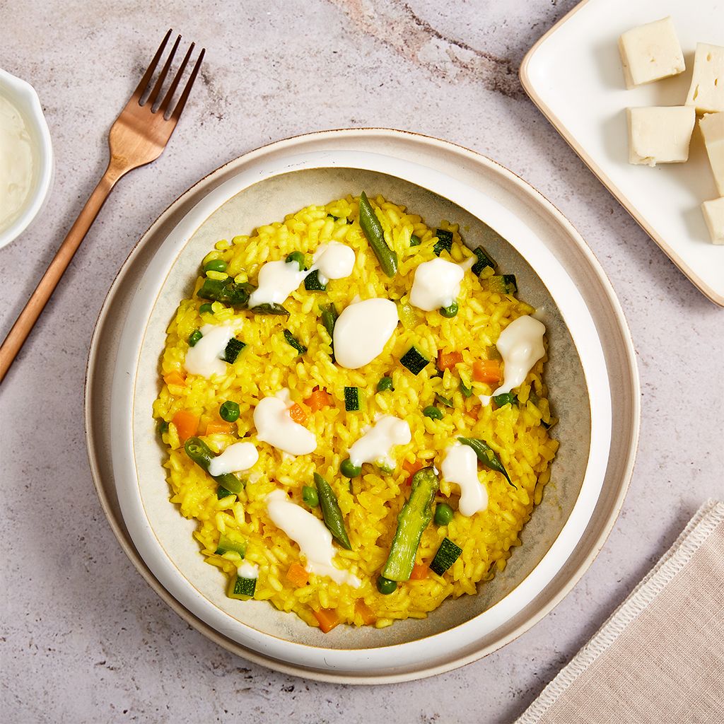 Creamy saffron risotto with asparagus and melted cheese served in a minimalist ceramic bowl