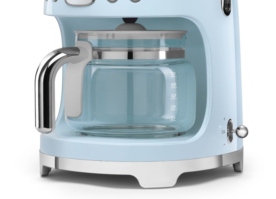 Close-up of the glass carafe with a chrome handle, sitting inside the base of a pastel blue drip filter coffee machine.