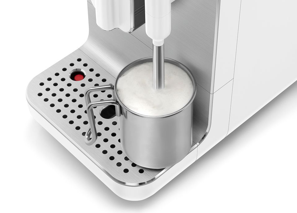 Close-up of stainless steel milk jug with frothed milk under Smeg coffee machine steam wand on drip tray