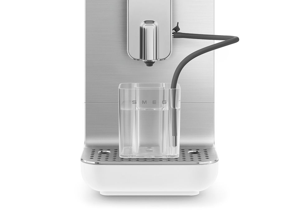 Empty glass milk container connected to Smeg coffee machine milk system with dispensing nozzle above drip tray