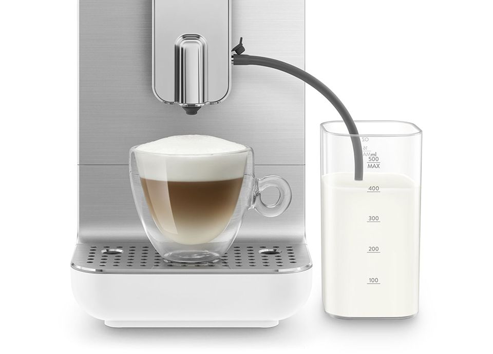 Glass cup of latte with frothed milk prepared by Smeg coffee machine milk system, connected to external milk container