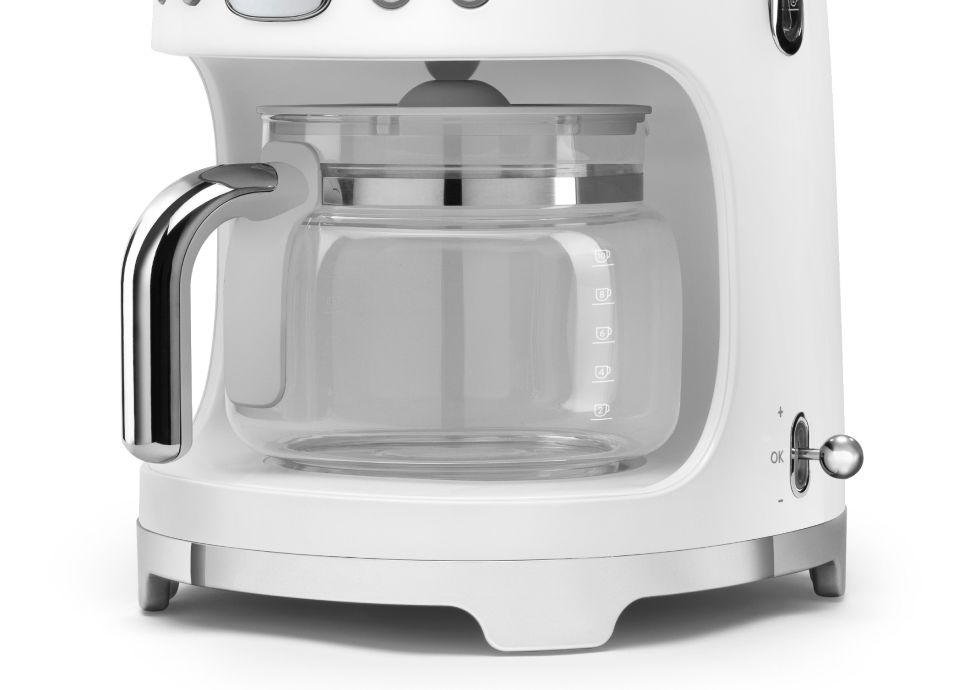 Primo piano della caraffa in vetro con manico cromato, posizionata all'interno della base di una macchina da caffè con finitura opaca.
