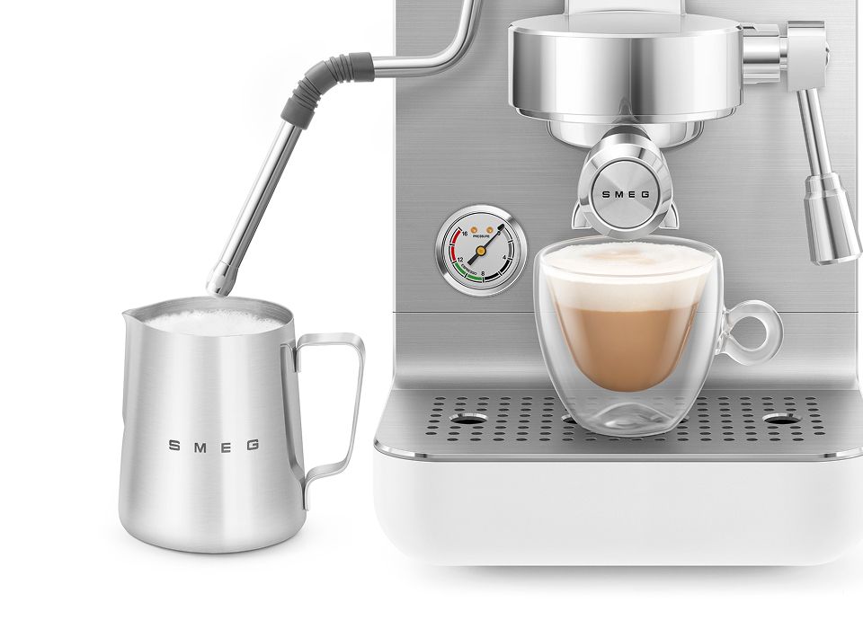 Stainless steel mini professional coffee machine with steam wand frothing milk in a metal jug and preparing a creamy latte