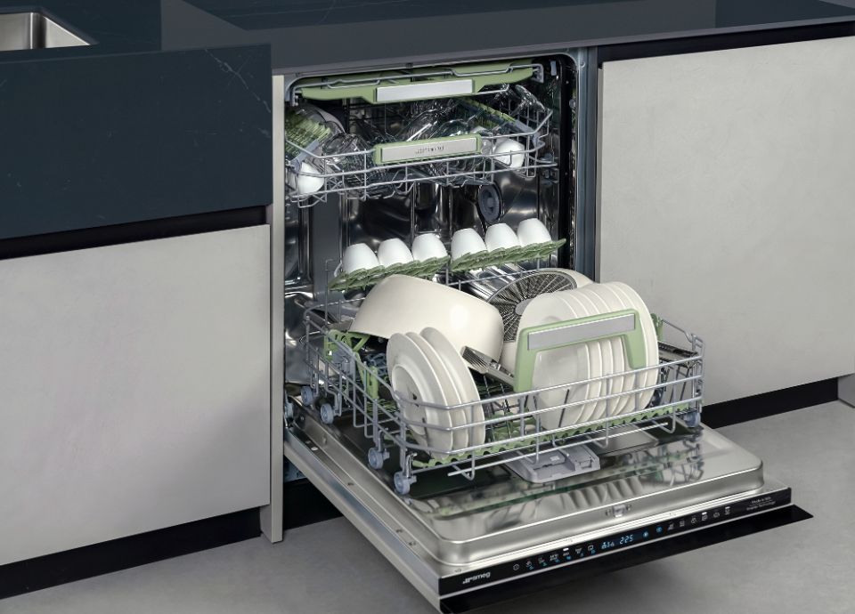 A Smeg dishwasher with its door open, revealing two racks fully loaded with dishes, cups, and cutlery.
