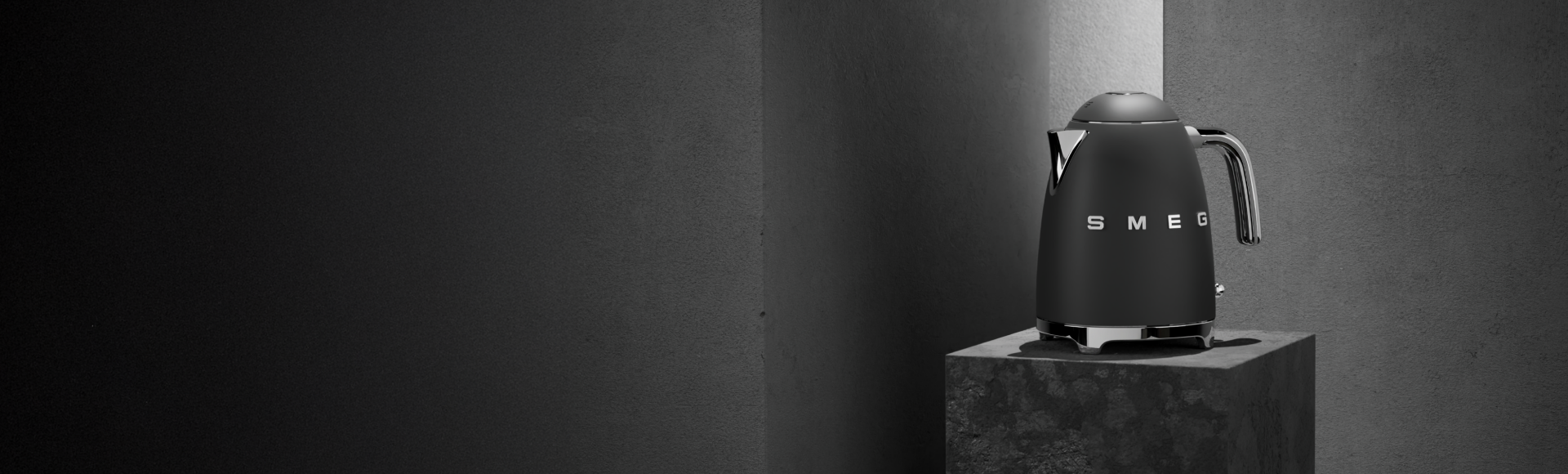 Matte black SMEG kettle placed on a stone pedestal in a dark, minimalist setting