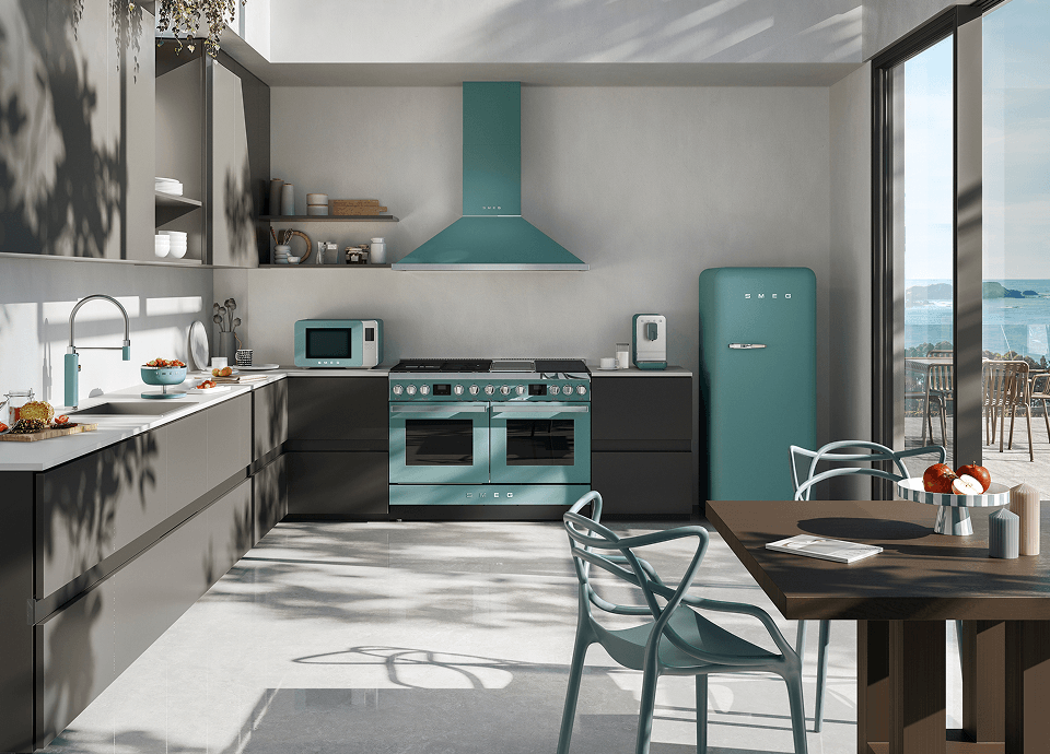 Cuisine moderne équipée d'appareils électroménagers SMEG au fini vert émeraude mat, comprenant une cuisinière, une hotte, un réfrigérateur et un micro-ondes, aménagée dans un espace lumineux doté de grandes fenêtres et d'un mobilier minimaliste