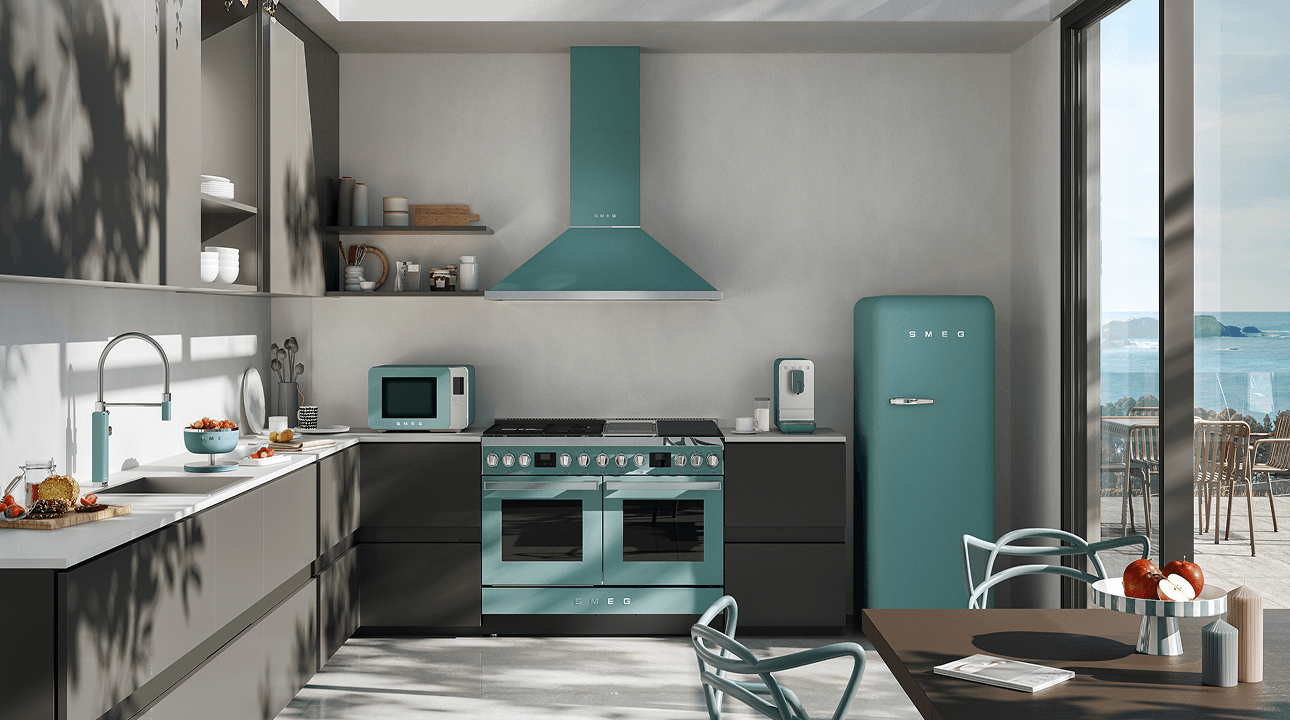 Modern kitchen interior featuring SMEG appliances with storm blue accents, including a cooker, extractor hood, and retro-style refrigerator, set against neutral cabinetry with natural light, plants, and a dining area.