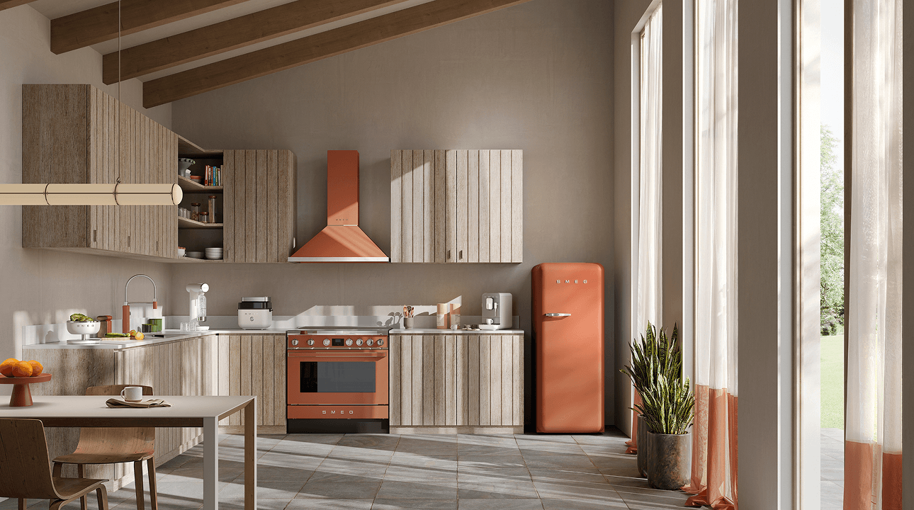 Minimalist kitchen with SMEG appliances in amber clay finish, including a range cooker, extractor hood, and retro-style refrigerator, set against light wood cabinetry, soft neutral walls, and natural light from a large window.
