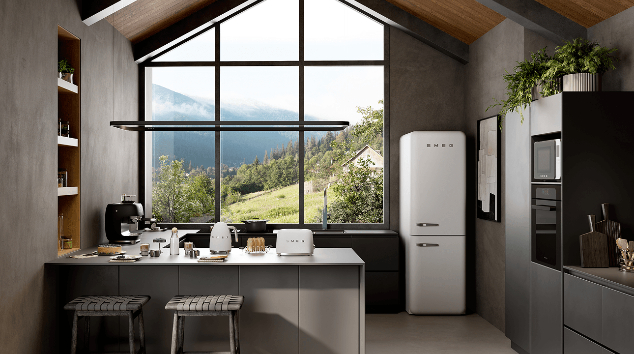 Modern kitchen with a high vaulted ceiling and large panoramic window overlooking a green mountain landscape, featuring SMEG appliances on a central island and a retro-style refrigerator, with neutral cabinetry, dark accents, and warm wood finishes.