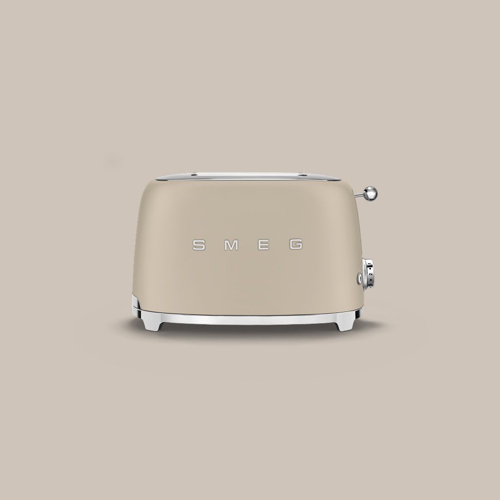 A Moonlight Smeg 50s Style 2-slice toaster with chrome accents sits on a textured stone block against a neutral wall