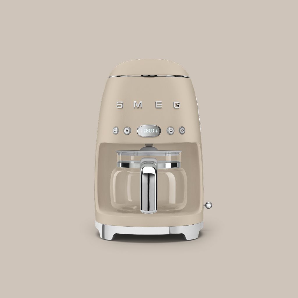A Moonlight Smeg 50s style filter coffee machine with a glass carafe sits on a stone plinth against a soft neutral background.