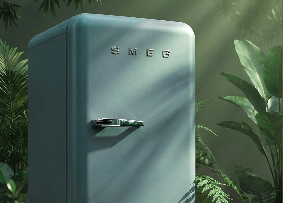 SMEG retro-style refrigerator in emerald green colour, featuring a smooth curved design and chrome handle, set among lush green plants with soft natural light creating leaf shadows across the surface.