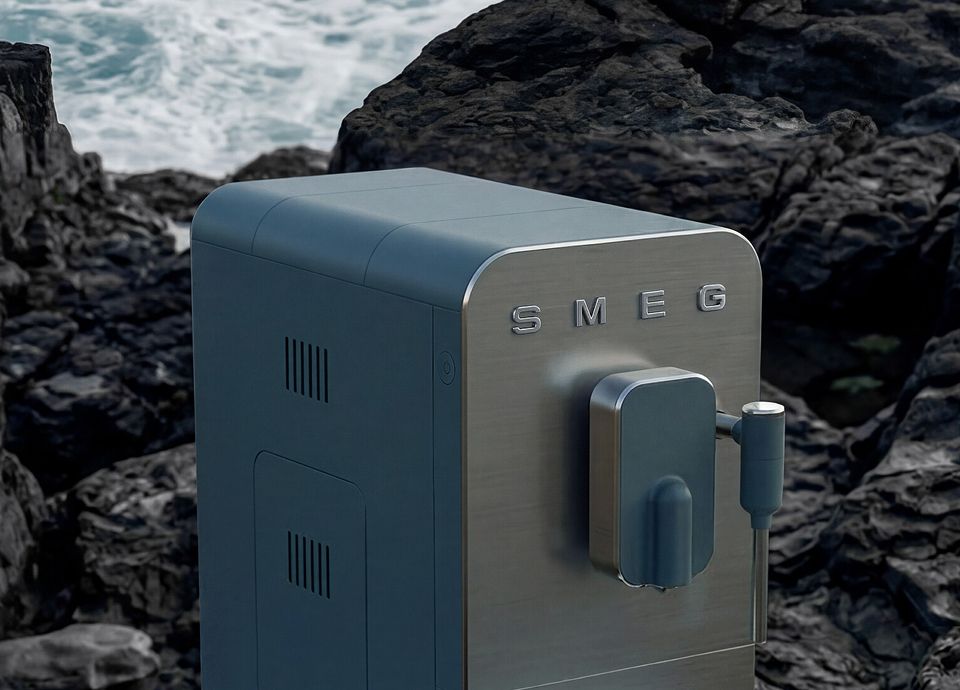 Storm blue SMEG coffee machine with stainless steel details, showcased among dark coastal rocks overlooking the sea.