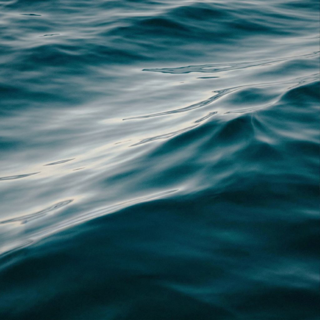 Close-up of storm blue water surface with gentle waves and soft light reflections creating a fluid, elegant texture.