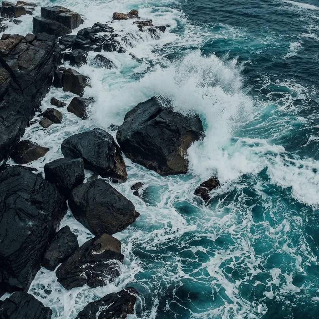 Powerful ocean waves crashing against dark coastal rocks, creating dramatic storm blue waters and dynamic white sea foam.