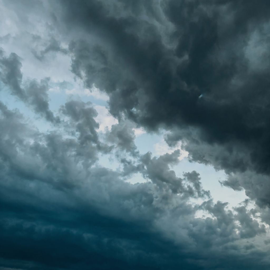 Dramatic storm blue sky filled with dark swirling clouds, creating a powerful contrast between deep shadows and soft light.