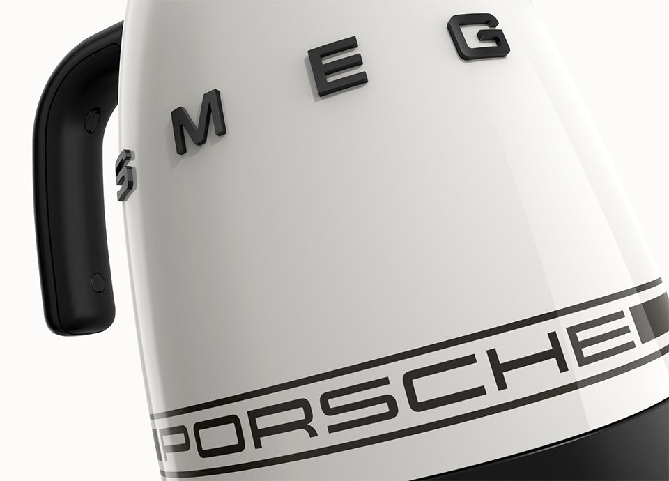 Particolare del bollitore in colore Carrara White. Il manico del bollitore è nero e il corpo centrale riporta il marchio "SMEG" in grassetto blu.ack uppercase letters. Near the bottom, a horizontal black band features the word "PORSCHE" in black uppercase letters.