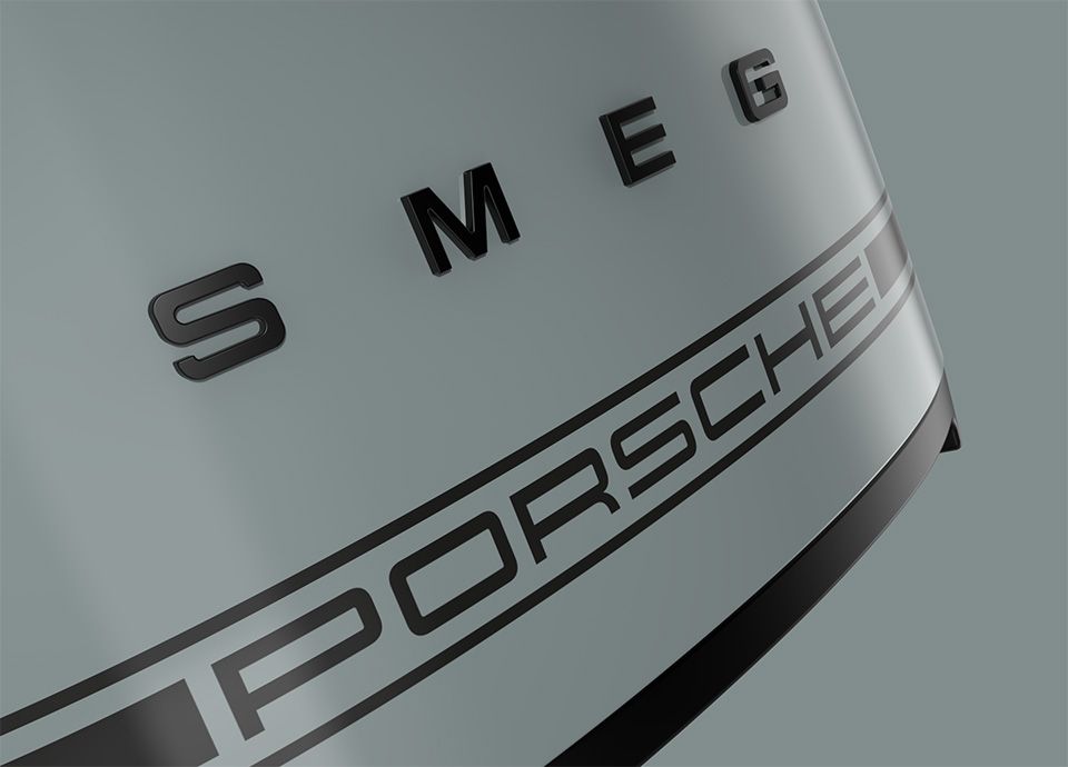 Dettaglio della parte anteriore del tostapane in tonalità verde. Sulla parte anteriore del tostapane è presente il marchio "SMEG" in grassetto e maiuscolo, mentre sotto di esso è presente un secondo logo con la scritta "PORSCHE", a indicare la collaborazione tra i due marchi.