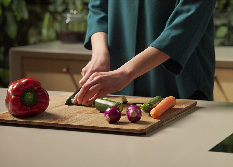 Person chopping zucchini, carrots, and bell peppers on a cutting board