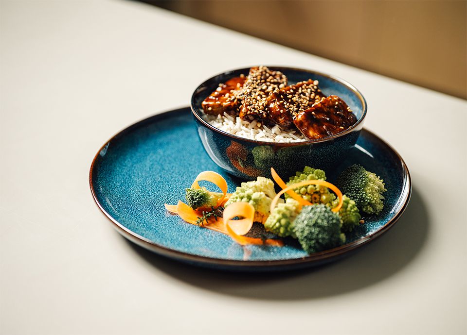 Tofu teriyaki served with sesame seeds and vegetables on a light blue ceramic plate
