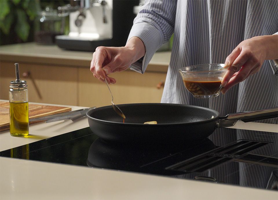 Adding prepared teriyaki sauce into a frying pan with tofu