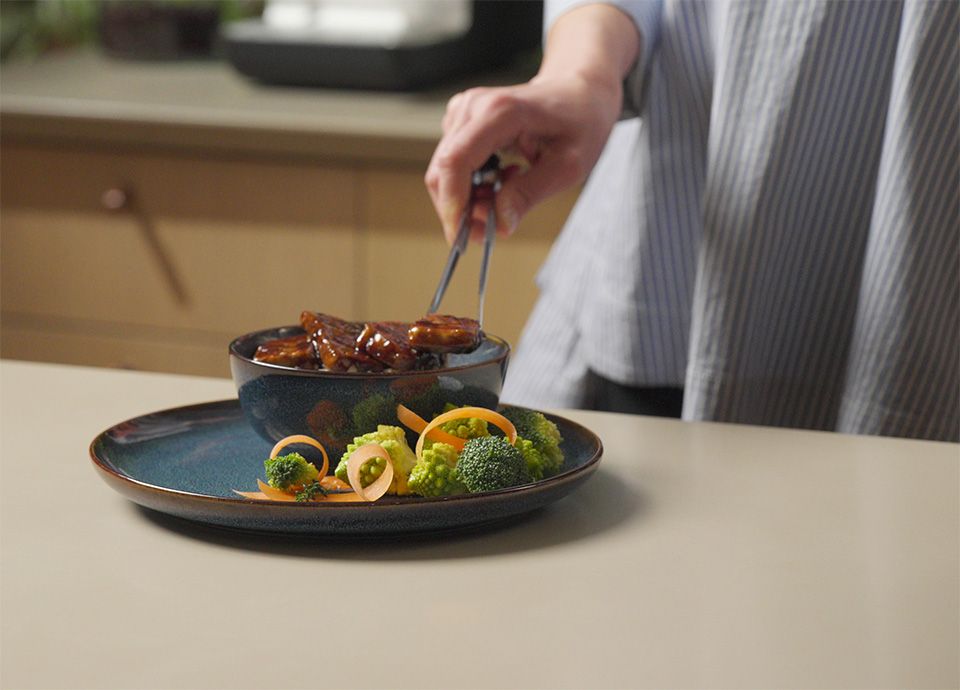 Person placing cooked tofu teriyaki onto a ceramic plate