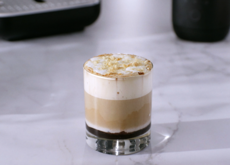 Glass of iced tiramisu caramel coffee with layered espresso, cold milk, and creamy milk foam topped with biscuit crumble.