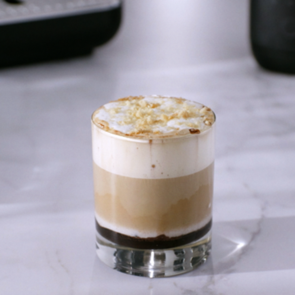Glass of iced tiramisu caramel coffee with layered espresso, cold milk, and creamy milk foam topped with biscuit crumble.