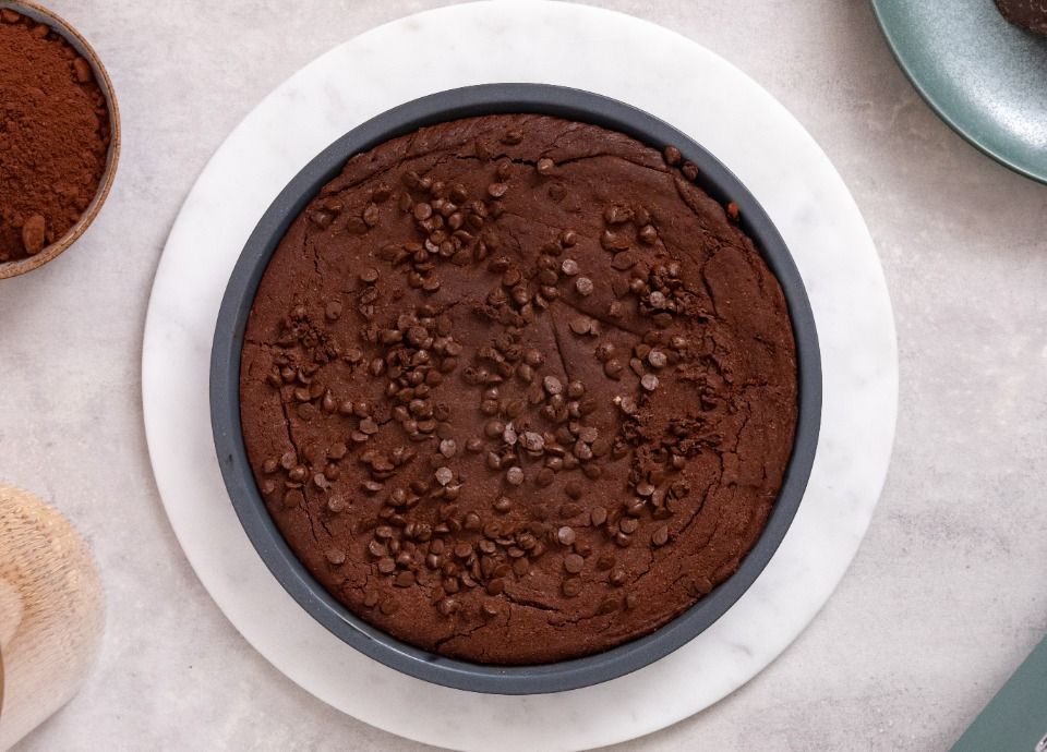 Top view of a chocolate brownie topped with chocolate chips in a round baking pan.