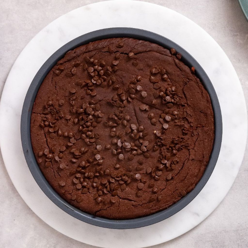 Top view of a chocolate brownie topped with chocolate chips in a round baking pan.