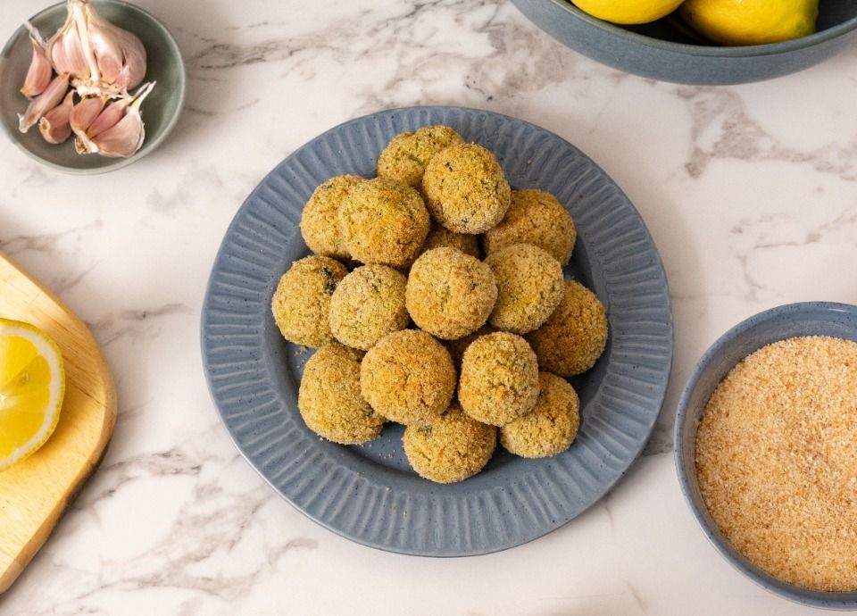 Homemade cod and zucchini meatballs on a serving plate with fresh zucchini, lemon and breadcrumbs, ready to cook.